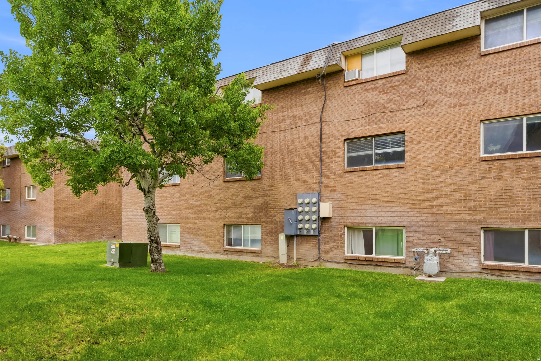 Brick exterior building with multiple windows, featuring a sloped roofline and a verdant lawn