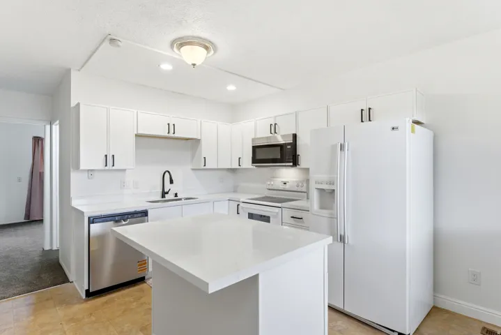 Bright kitchen featuring white cabinetry with dark pulls, white countertops, stainless steel dishwasher, and a center island