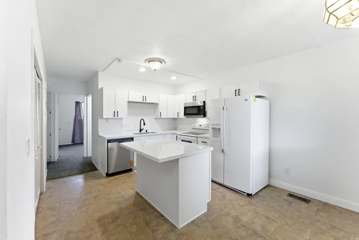 Modern kitchen featuring white cabinetry with black hardware, a center island with a white countertop, stainless steel dishwasher, and a black faucet