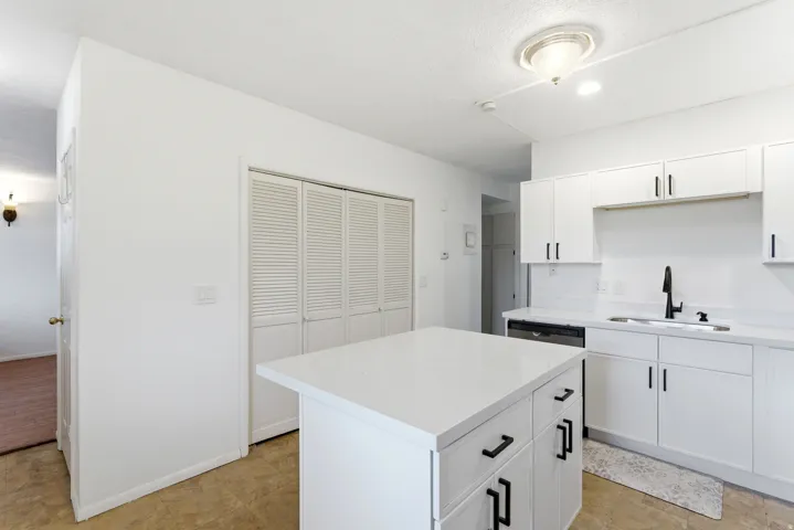 Modern kitchen featuring a central island with white countertop, white cabinetry with black hardware, a stainless steel dishwasher, and a black faucet