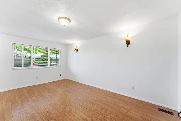 Spacious room featuring wood-finish flooring, white walls, and a large window with horizontal blinds
