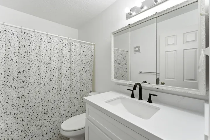 Bathroom featuring a white vanity with an integrated sink, matte black faucet, and a wall-mounted mirrored medicine cabinet with integrated lighting