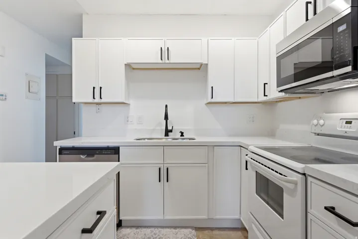 Contemporary kitchen with white cabinetry, matte black hardware, light countertops, and stainless steel appliances including an over-the-range microwave and dishwasher