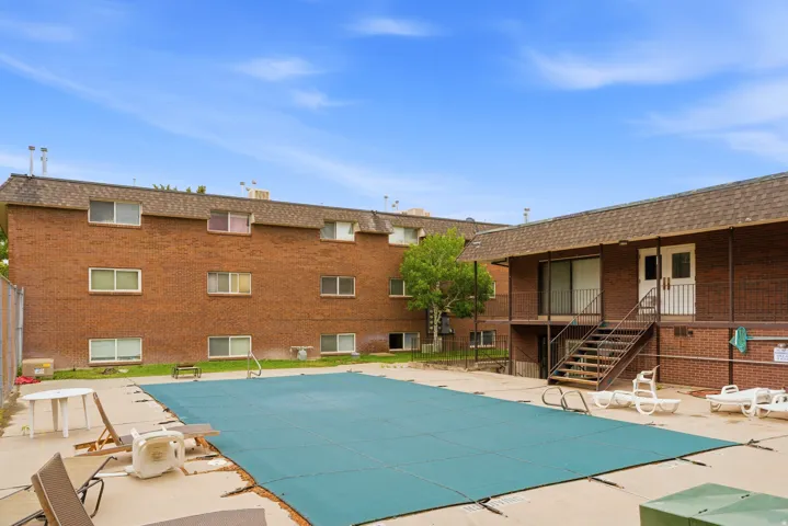Outdoor swimming pool area with a covered pool, concrete surround, and brick building with multiple windows