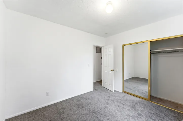 Bedroom featuring gray carpet, white painted walls, a standard white door, a ceiling-mounted light fixture, and a mirrored closet with gold-tone framing