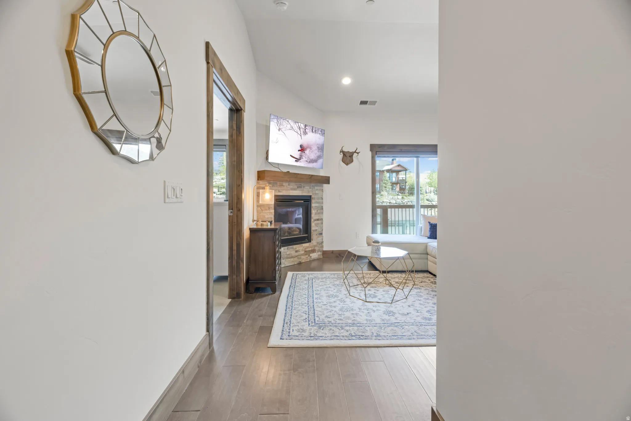 Living area featuring wood-finish flooring, a stone-faced fireplace with a wood mantel, and an exposed wood door frame