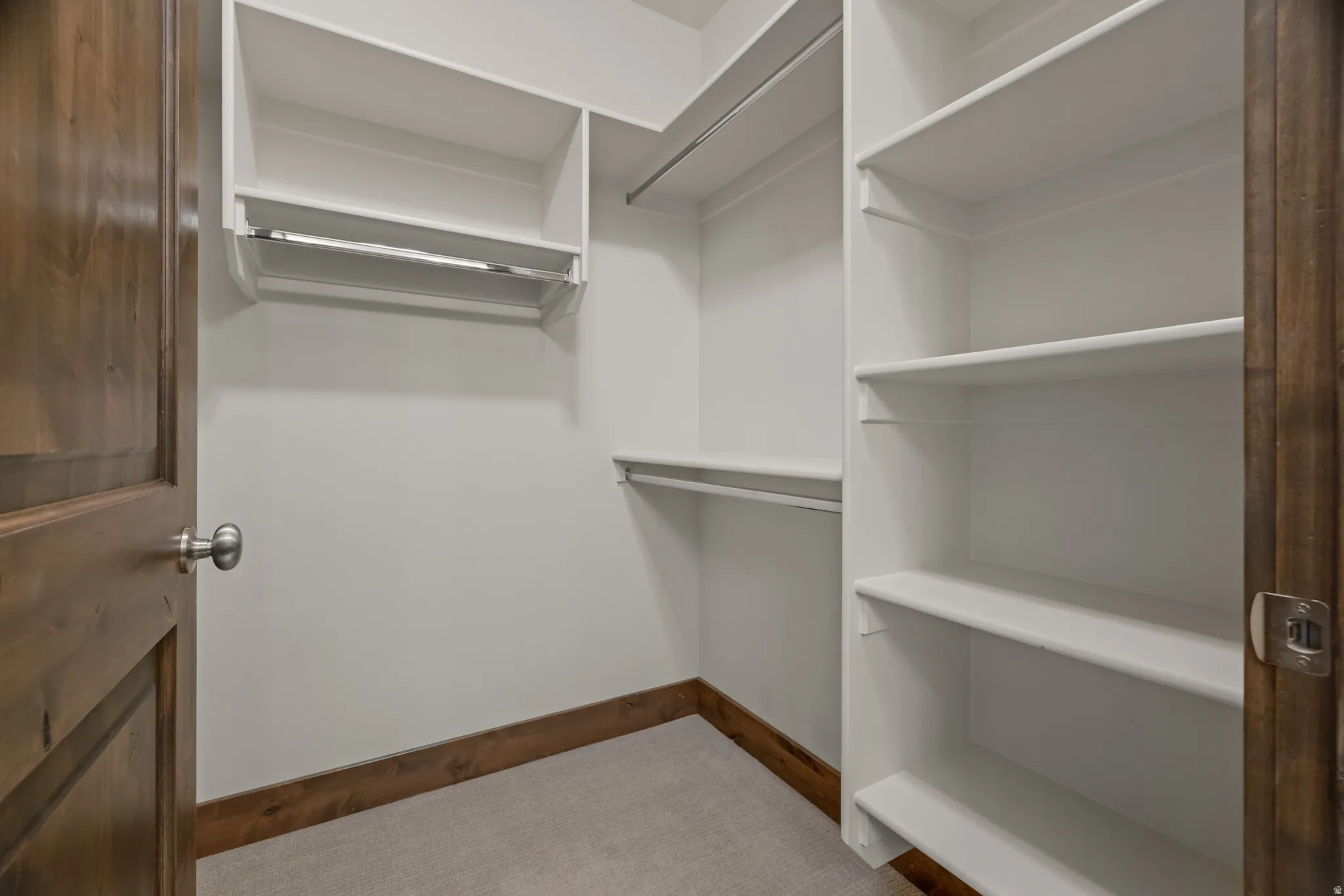 Walk-in closet featuring white built-in shelving, chrome hanging rods, and a wood-finish door