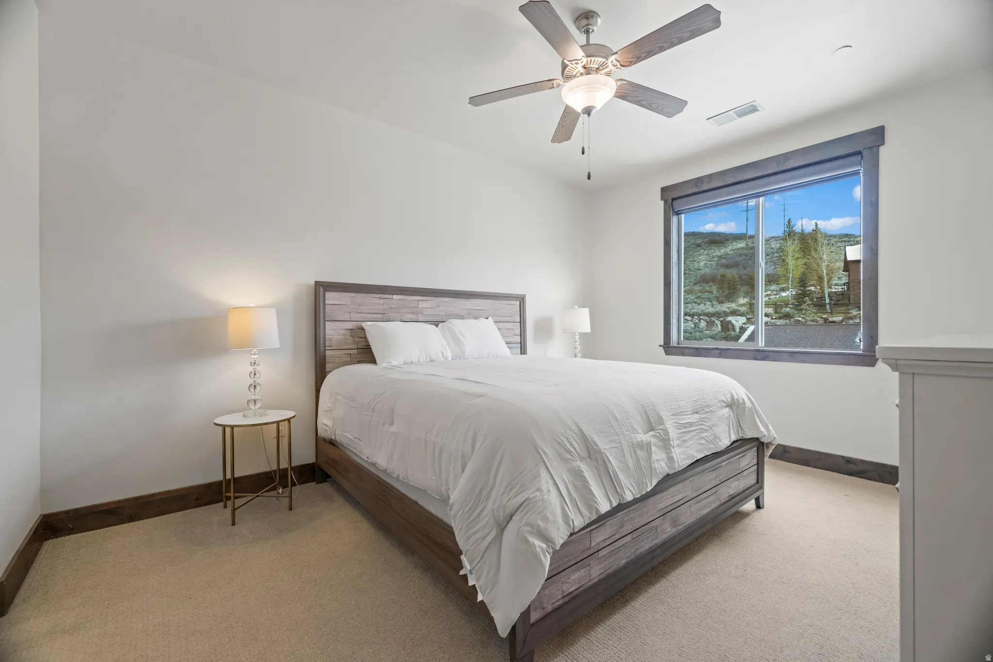 Bedroom featuring a large window with mountain scenery, a ceiling fan with integrated lighting, wood-finish baseboards, and neutral carpeting