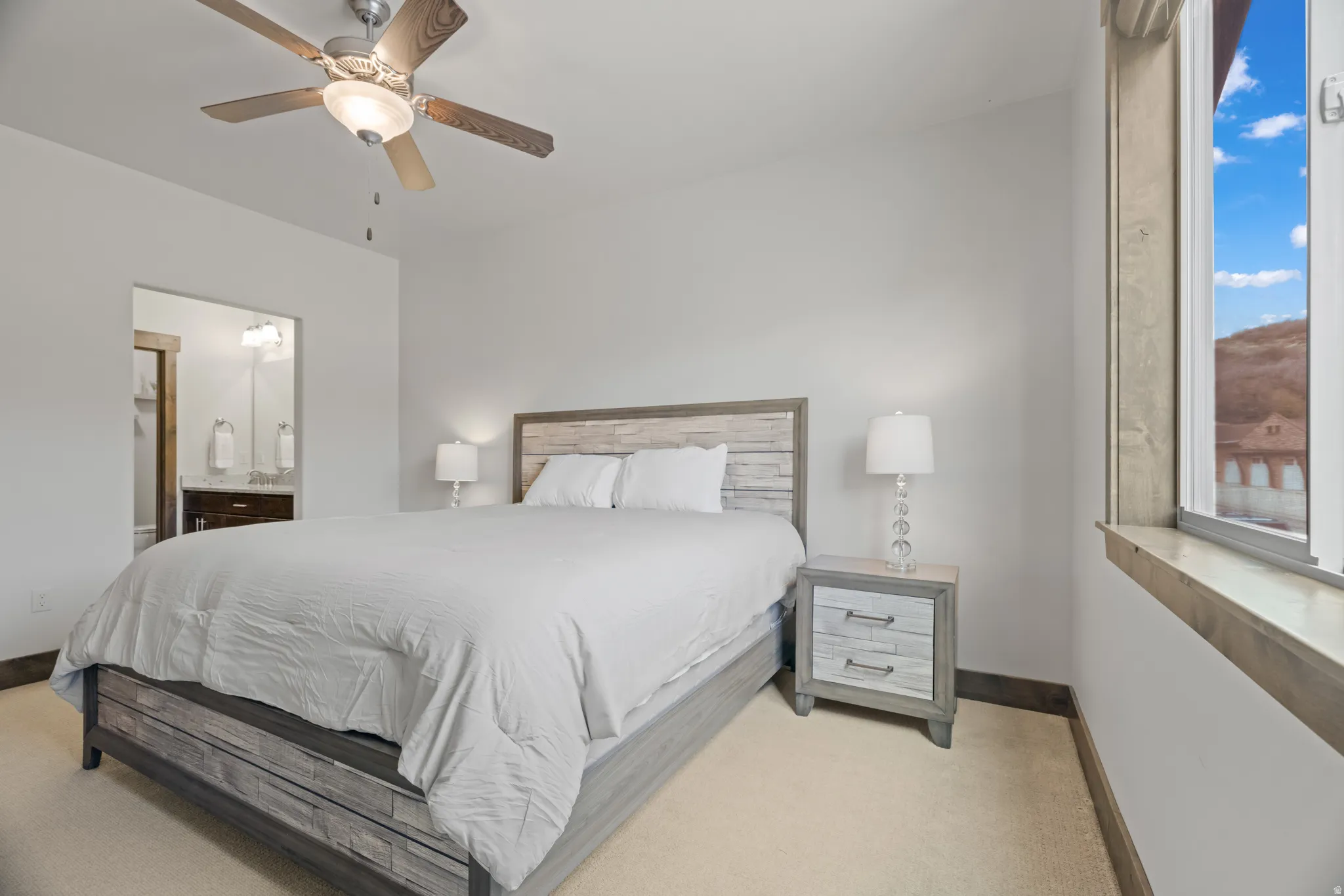 Neutral toned bedroom featuring a wood-finish ceiling fan and a window with wood trim