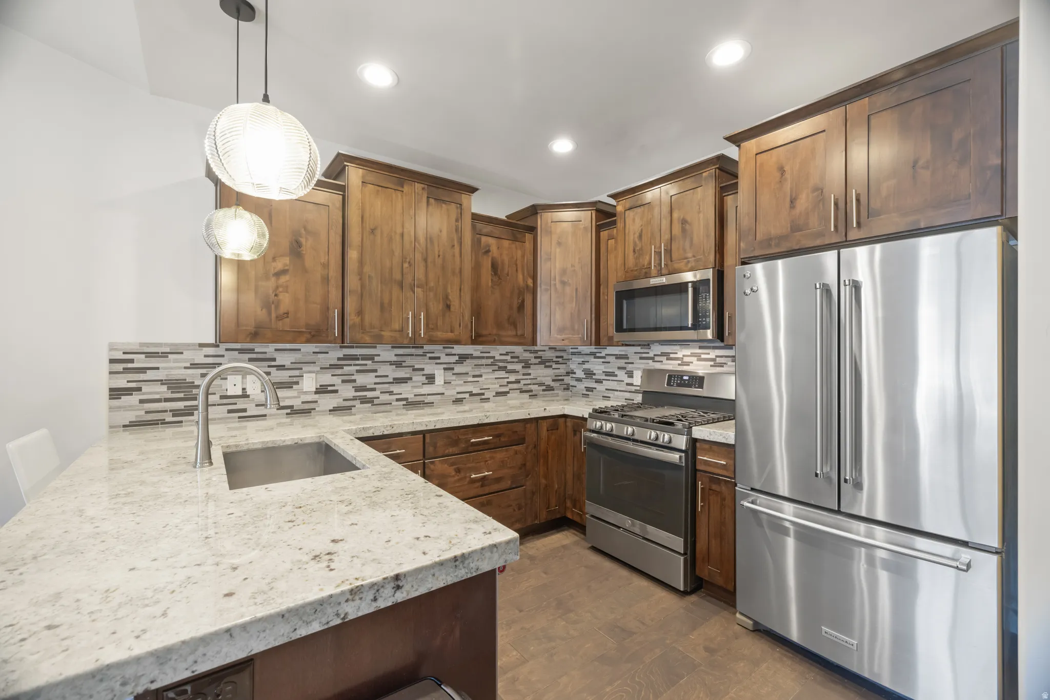 Kitchen featuring granite countertops, stainless steel appliances, wood cabinetry, mosaic tile backsplash, and recessed lighting