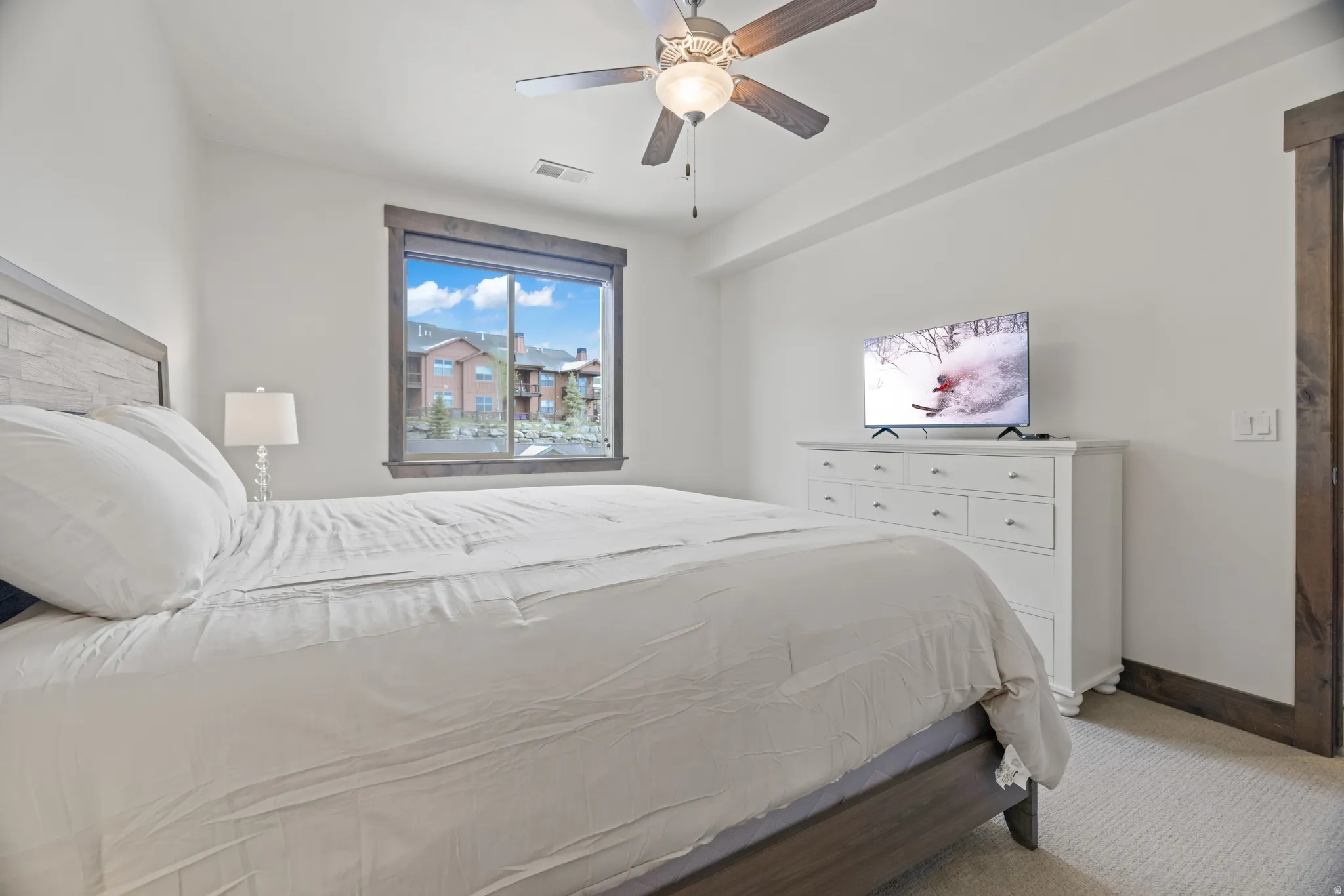 Spacious room featuring a large window with exterior views, wood-finish window trim, a ceiling fan with integrated lighting, and neutral carpeting