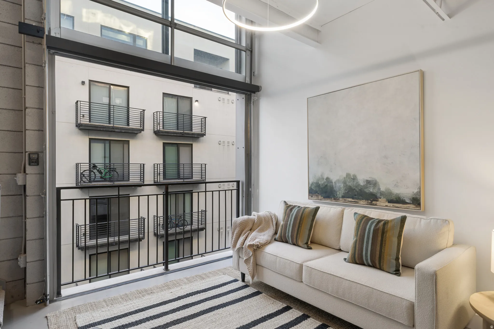 Double-height living area with expansive full-height windows, concrete flooring, and a modern circular pendant light fixture