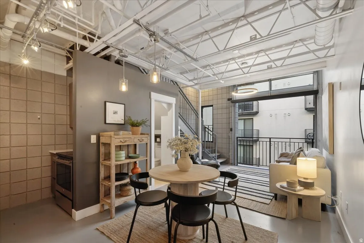 Open-concept living space featuring exposed ceiling joists, track lighting, a full-height glass roll-up door, and industrial-style stairs with open risers
