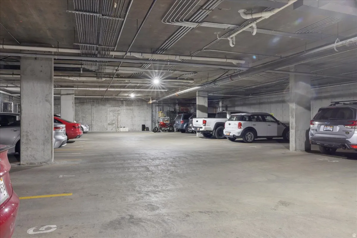 Underground parking garage featuring concrete flooring, exposed overhead conduits, and overhead lighting
