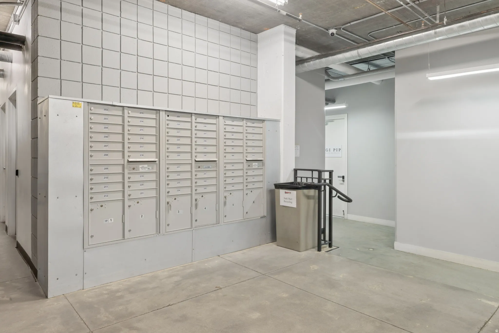 Mail room featuring a bank of individual mailboxes, exposed conduit ceiling, concrete flooring, and tiled wall accents