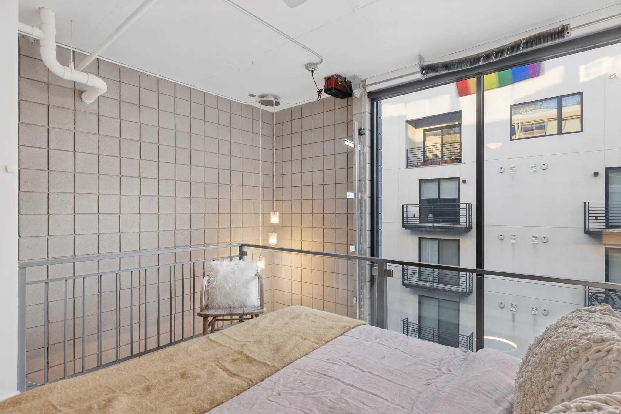 Loft-style space featuring a full-height window, industrial-style railings, exposed ceiling pipes, and a textured accent wall
