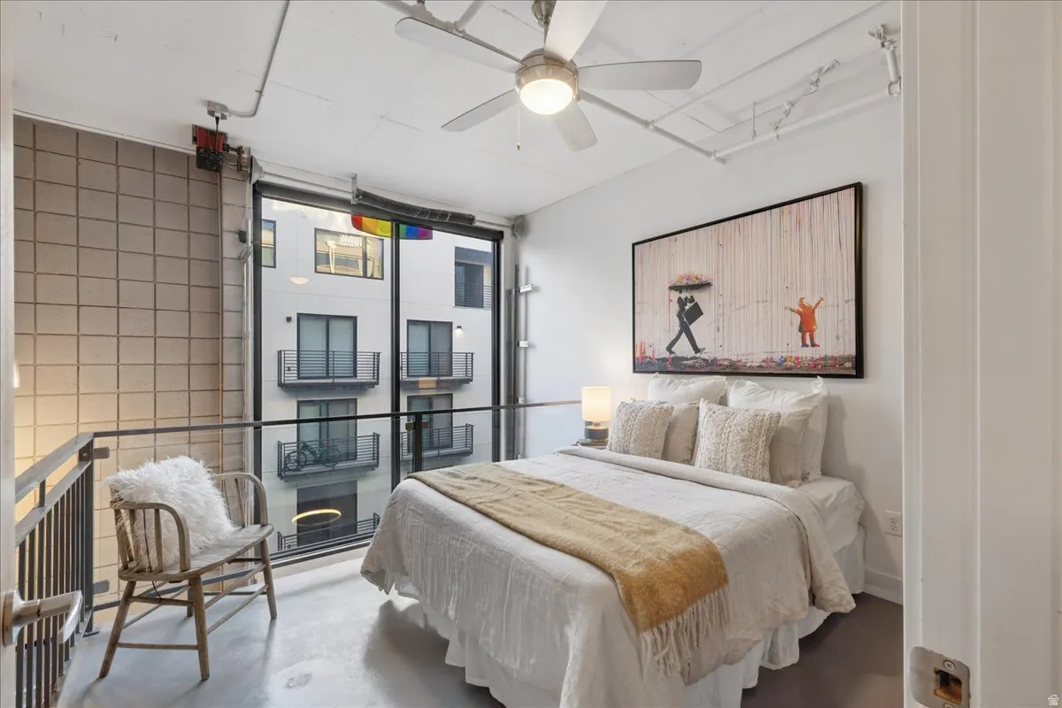 Loft bedroom featuring a full-height window, concrete flooring, exposed ceiling conduit, and a ceiling fan with integrated lighting