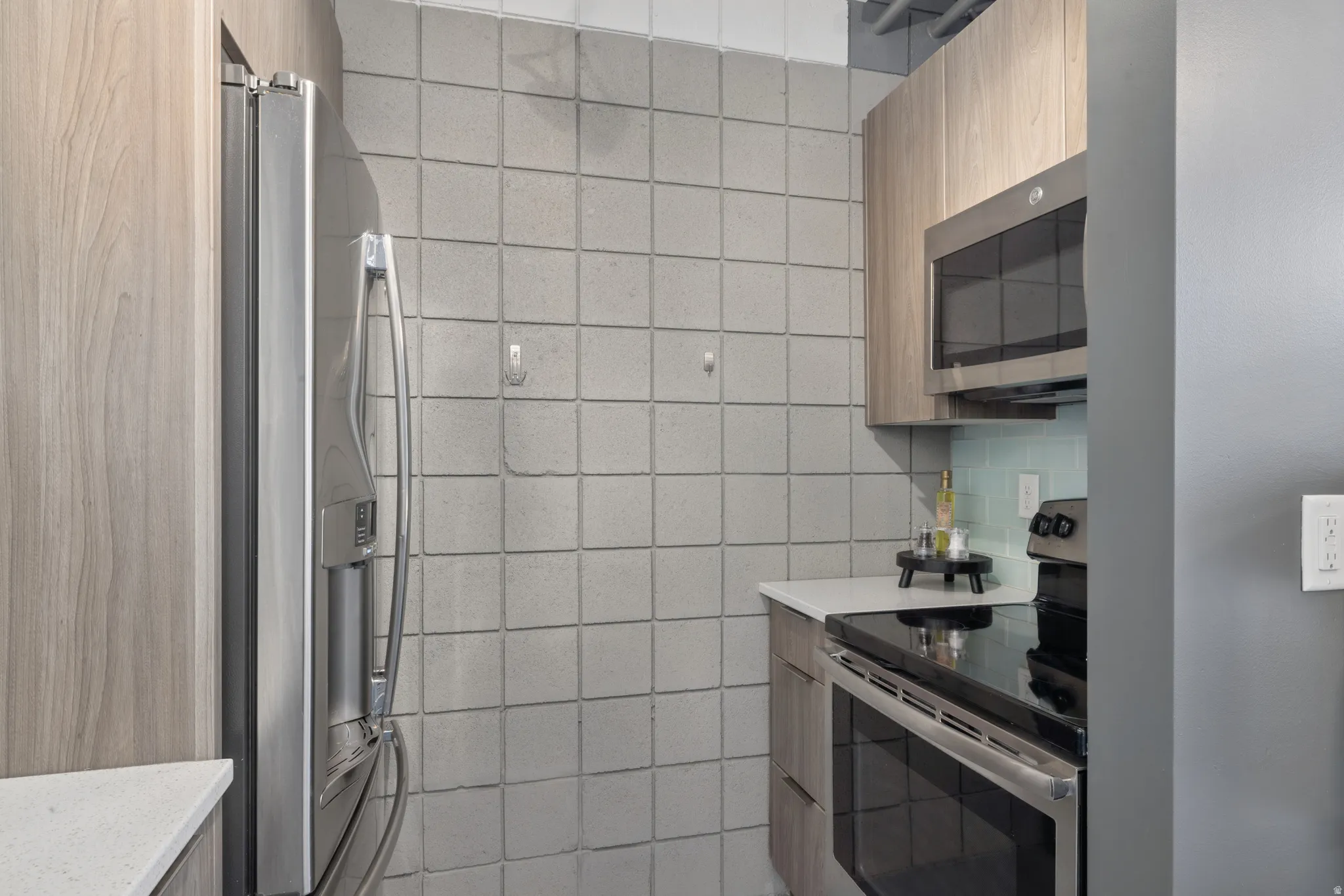 Kitchen featuring stainless steel appliances, wood-finish cabinetry, white countertops, and a light blue tile backsplash