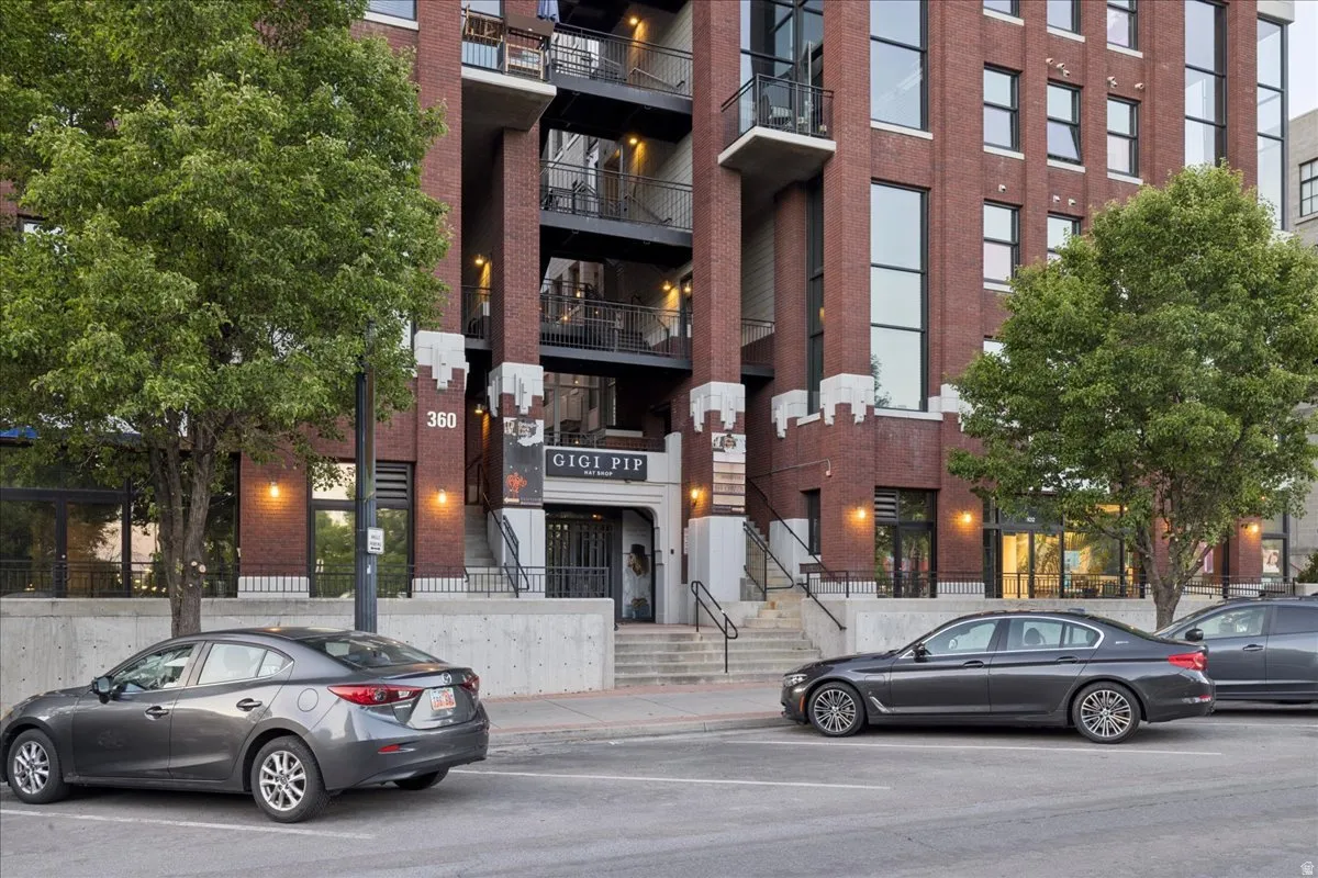 Brick facade building featuring a prominent entrance with "GIGI PIP" signage, visible street parking, mature trees, ground-level commercial spaces, and residential balconies on upper floors