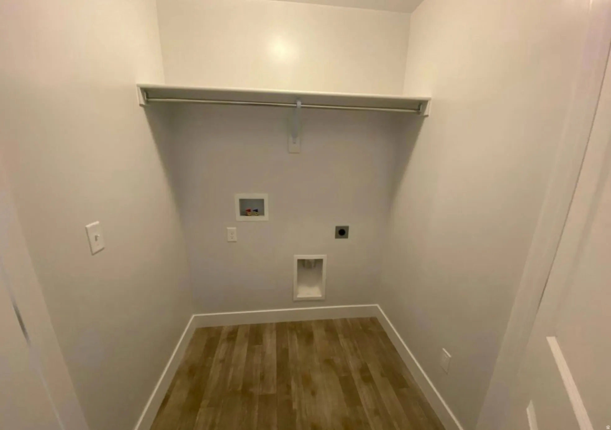 Dedicated utility space featuring wood-finish flooring, light-colored walls, and a built-in shelving unit with a hanging rod