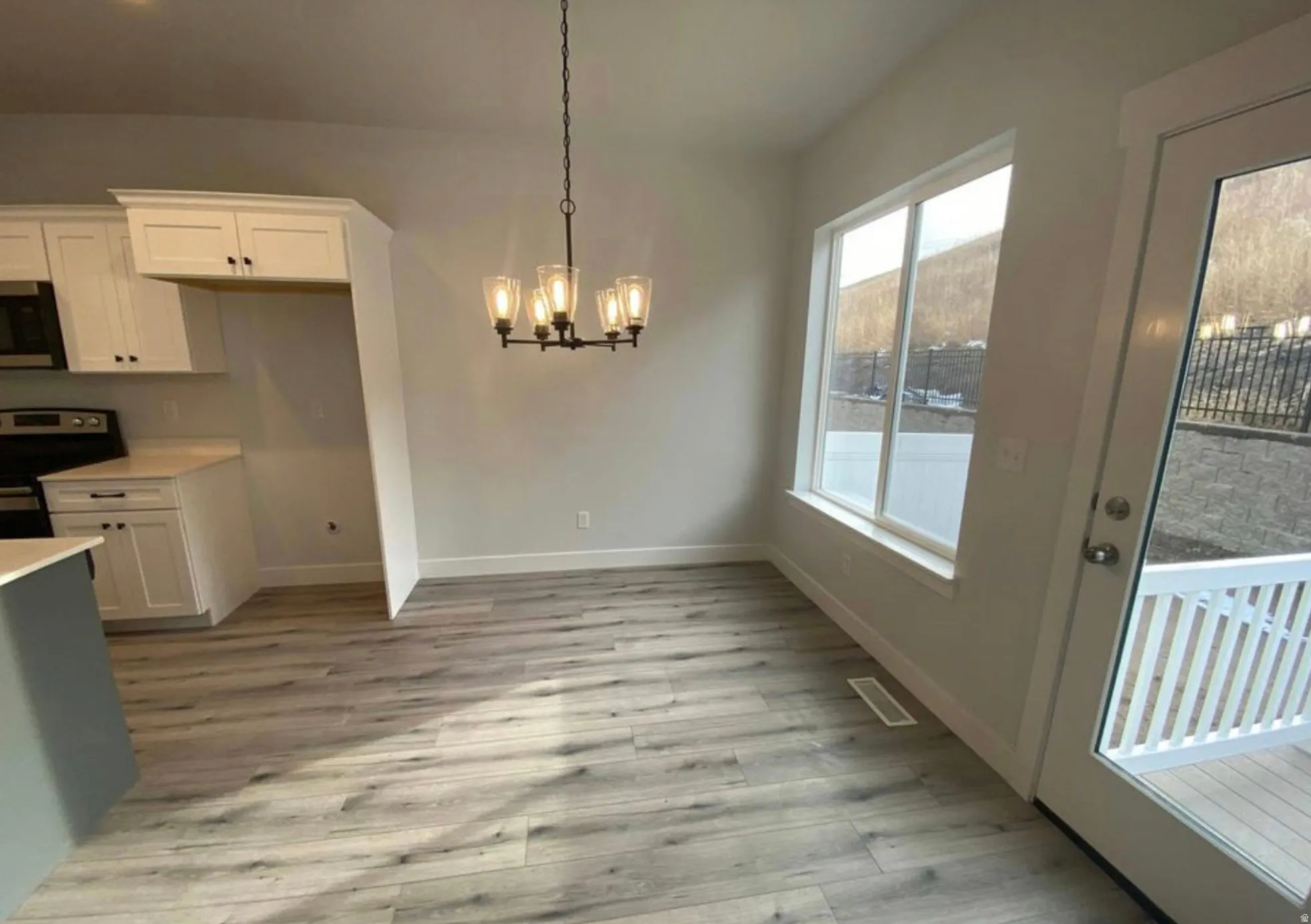 Open-concept dining area with wood-finish flooring, a contemporary chandelier, and large windows