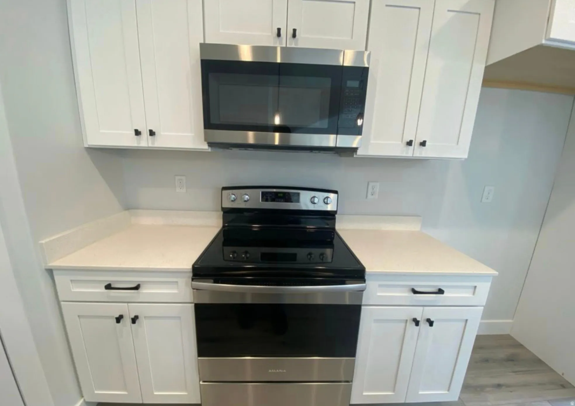 Kitchen featuring a stainless steel electric range, over-the-range microwave, white shaker-style cabinetry, dark cabinet hardware, and light-toned countertops