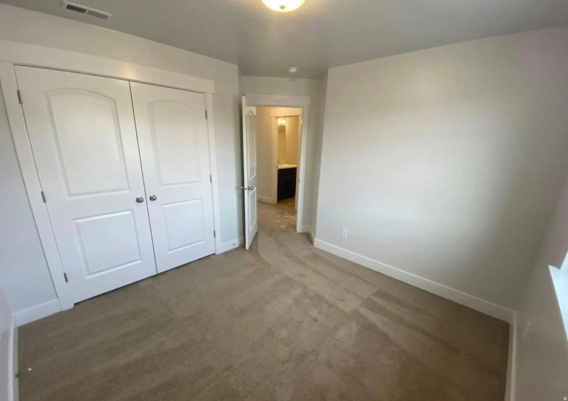 Bedroom featuring light-toned carpeting, white baseboards, and a pair of white paneled bifold closet doors