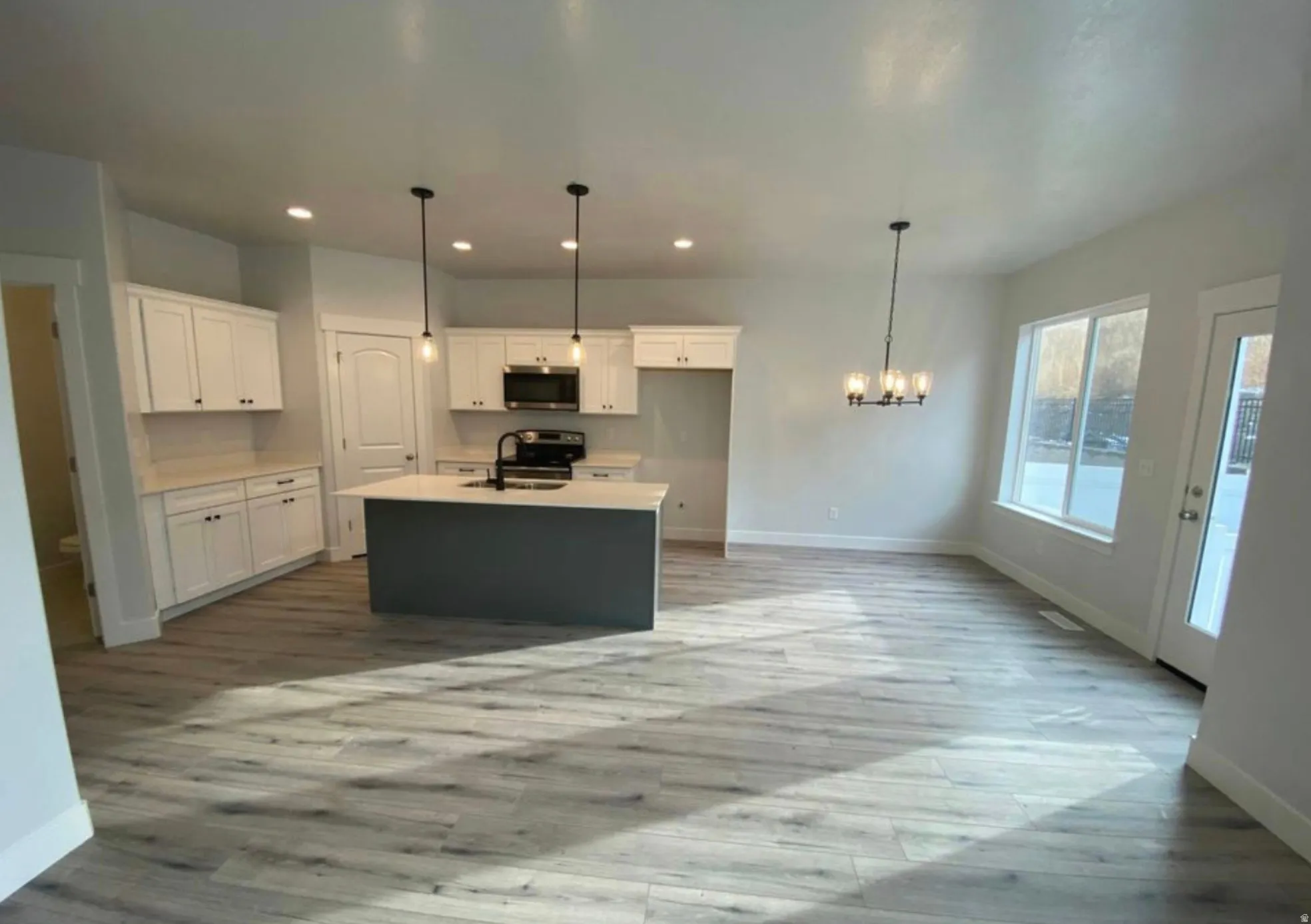 Bright, open-concept kitchen and dining area featuring a dark gray island, white cabinetry, a black appliance suite, and light wood-finish flooring