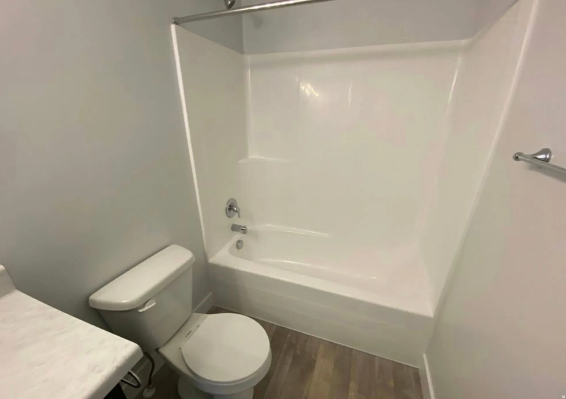 Full bathtub with integrated shower, white toilet, and wood-finish flooring