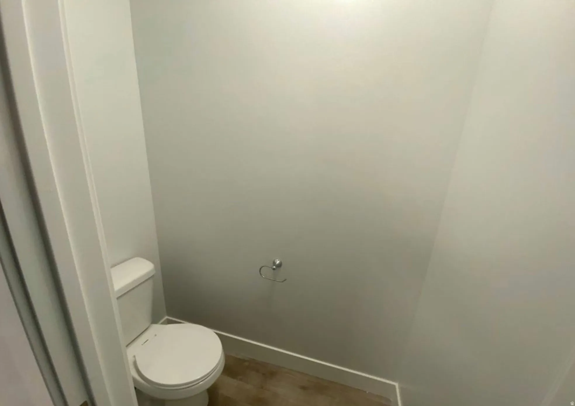 Water closet featuring a white toilet, light gray walls, white baseboards, and wood-finish flooring