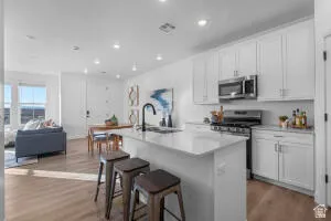 Open-concept living space with wood-finish flooring, white cabinetry, stainless steel appliances, a kitchen island, and recessed lighting