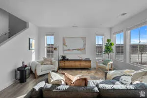 Expansive living area featuring large windows, wood-finish flooring, and a staircase with a modern handrail
