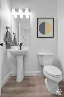 Powder room featuring a pedestal sink with a single-handle faucet, a wall-mounted mirror, overhead vanity lighting, and wood-finish flooring