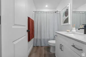 Bathroom featuring wood-finish flooring, a white vanity with a light-colored countertop, a sink with a matte black faucet, and a mirror