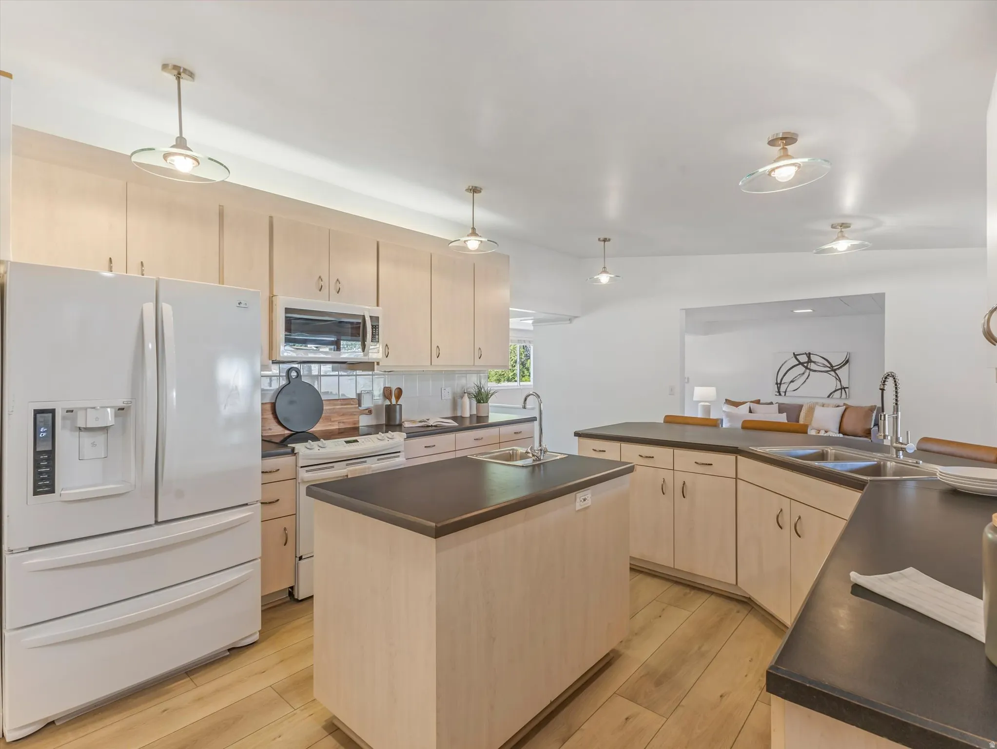 Kitchen featuring light wood-finish cabinetry, dark countertops, a central island, stainless steel double basin sink, and wood-finish flooring
