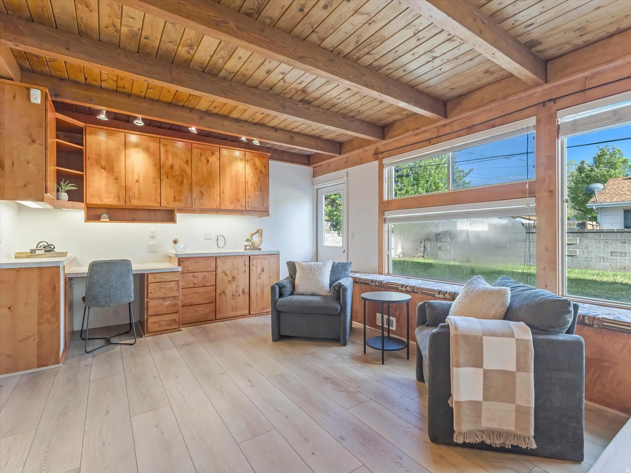 Spacious office/den space with french doors featuring a beamed wood ceiling, extensive built-in cabinetry with under-cabinet lighting, and light wood-finish flooring