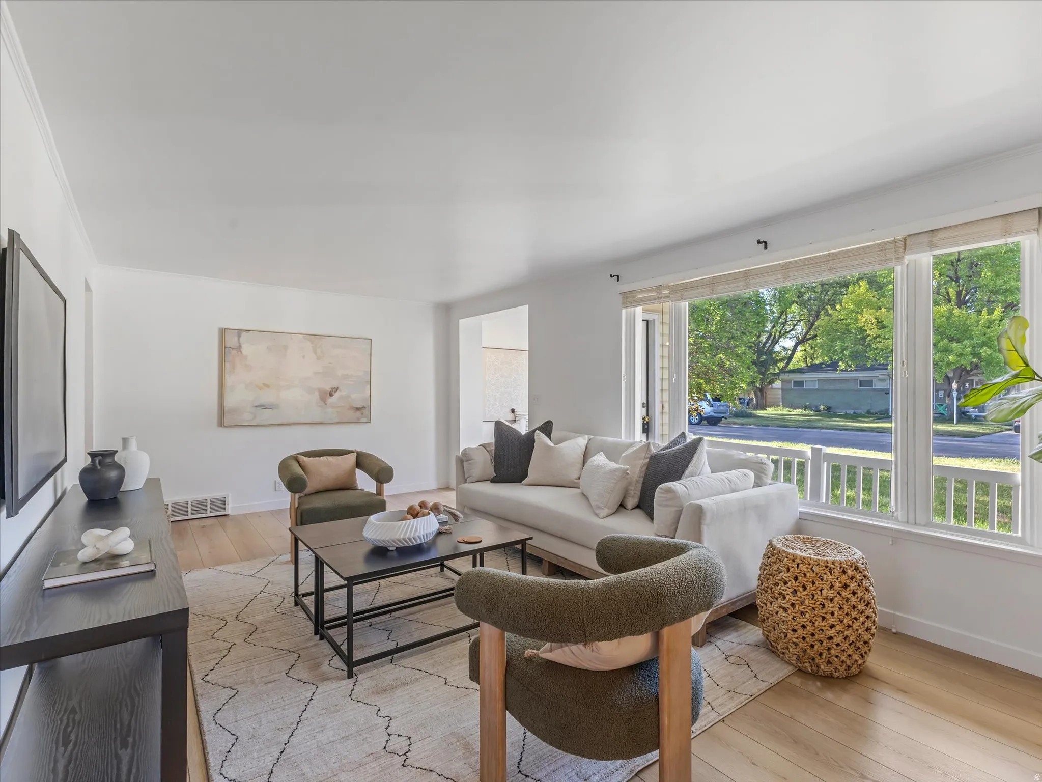 Bright living space featuring wood-finish flooring, a large multi-pane window, and white crown molding