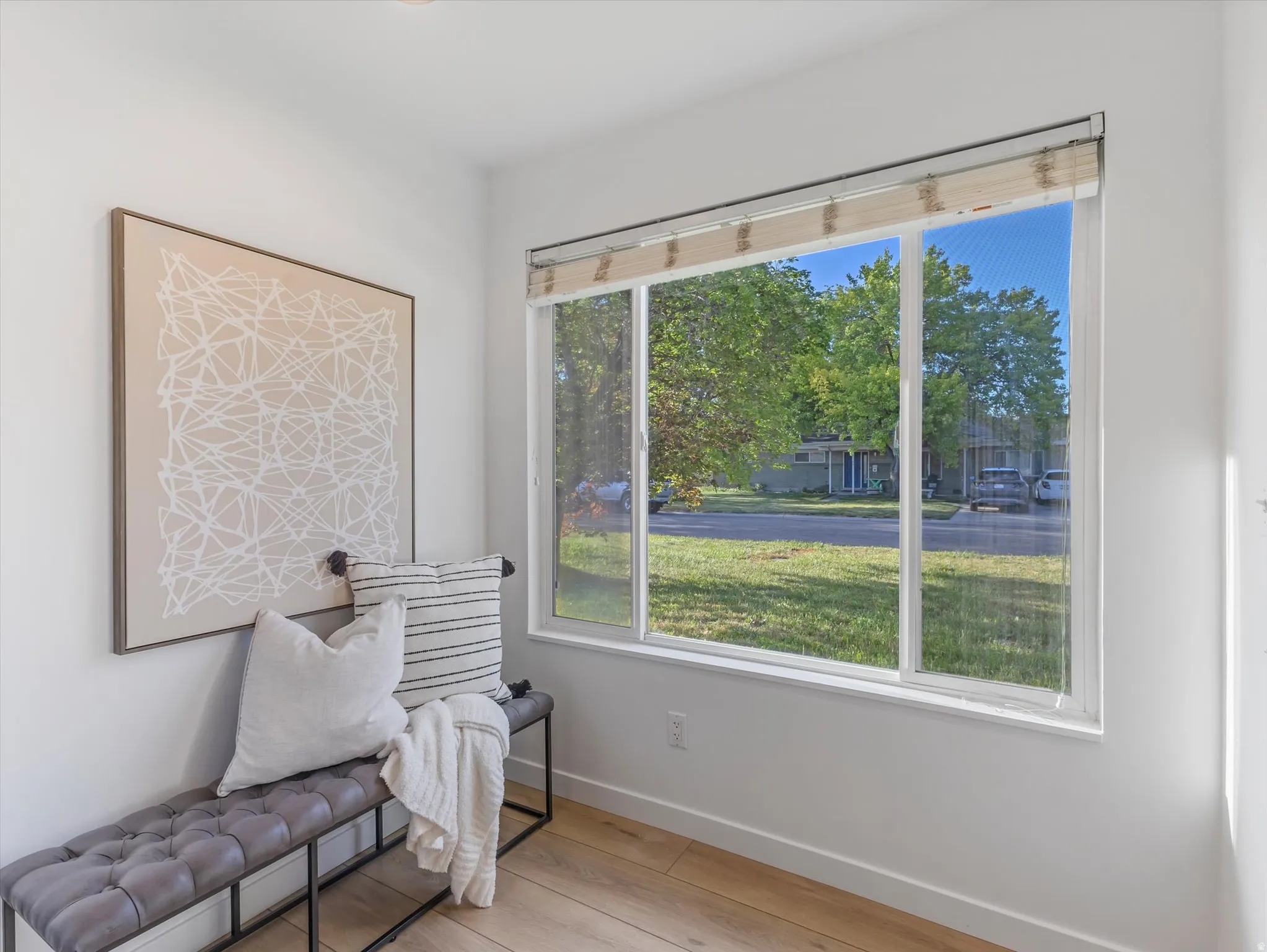 Bright interior entry space with wood-finish flooring, a large window with blinds, and white baseboards