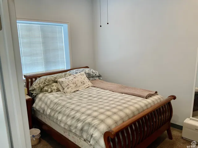 Bedroom featuring light-toned walls, a window with horizontal blinds, and a built-in ceiling fan with pull chains
