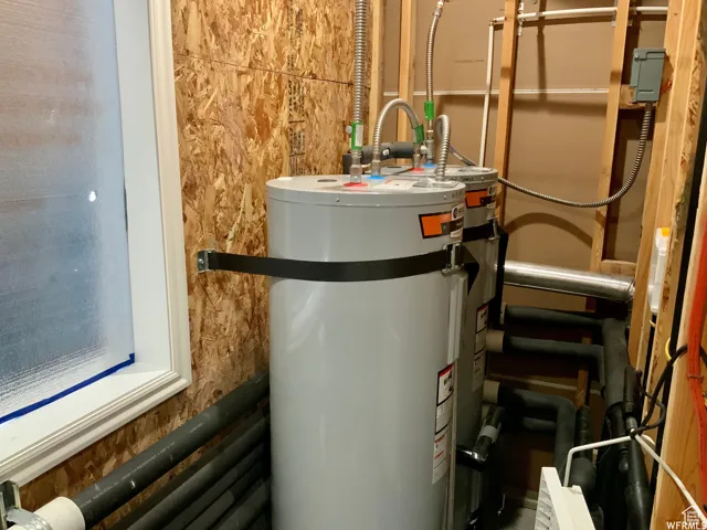 Utility space featuring two water heaters, exposed wood-finish paneling, white-framed window, and various visible plumbing and electrical components