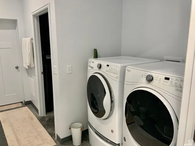 Dedicated laundry area featuring a front-loading washer and dryer, light gray walls, and a durable flooring surface