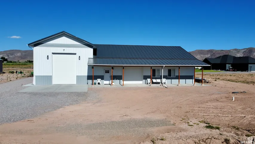 Modern construction featuring a metal roof, white and gray siding, an expansive gravel driveway, a covered porch, and a large roll-up garage door