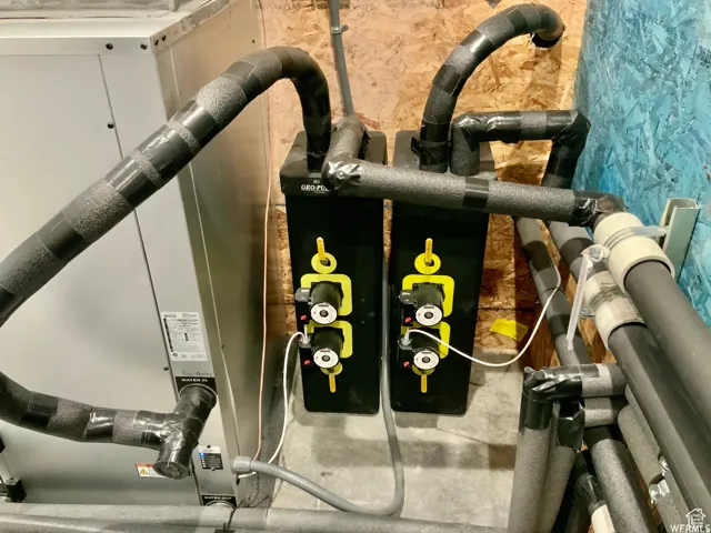 Utility area featuring a water heater, insulated piping, and two black control units with yellow accents