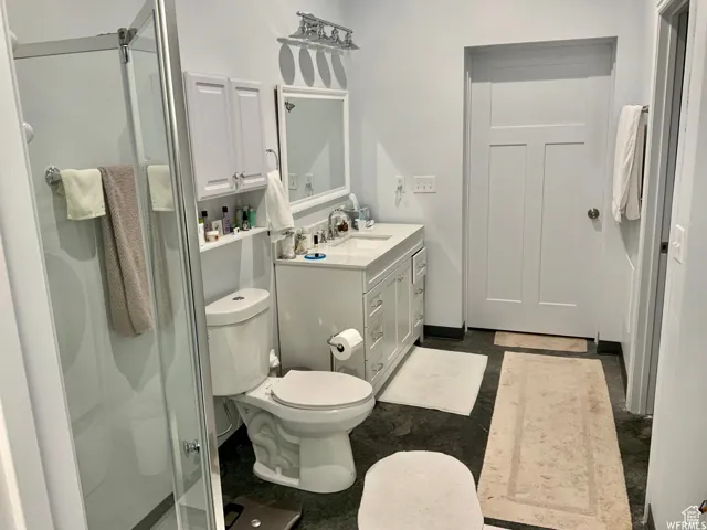 Bathroom featuring a glass-enclosed shower, single vanity with a white cabinet, and dark-toned flooring