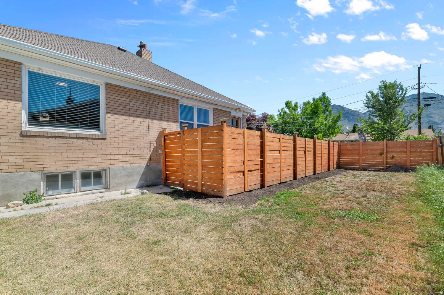 Expansive backyard featuring a new horizontal slat wood fence, brick exterior, and multiple windows