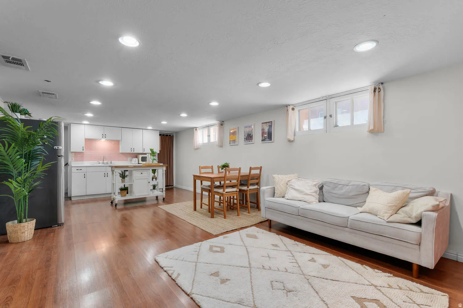 Open-concept living space featuring wood-finish flooring, recessed lighting, and a white kitchen with a pink tile backsplash