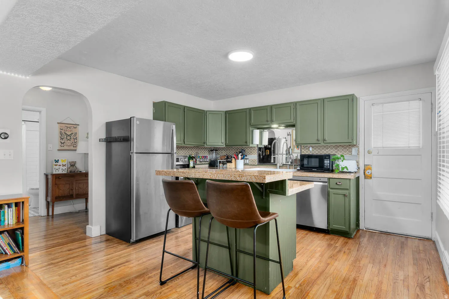 Kitchen featuring sage green cabinetry, stainless steel appliances, a breakfast bar with stone-finish countertop, and wood-finish flooring