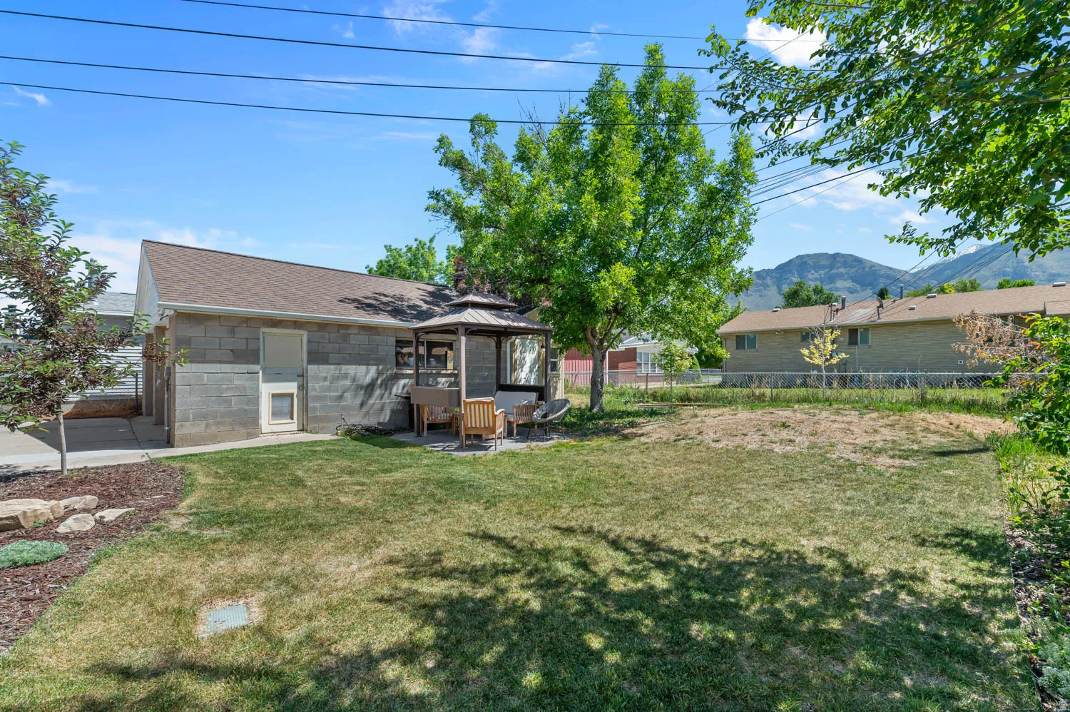Expansive backyard featuring a concrete block exterior, a detached gazebo with a metal roof, mature trees, and a mountain backdrop