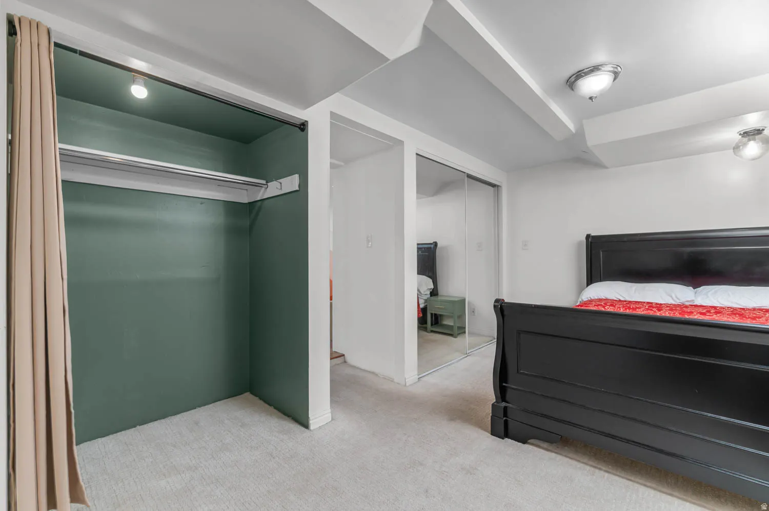 Carpeted room featuring a built-in closet with green interior walls, overhead lighting, and a clothing rod