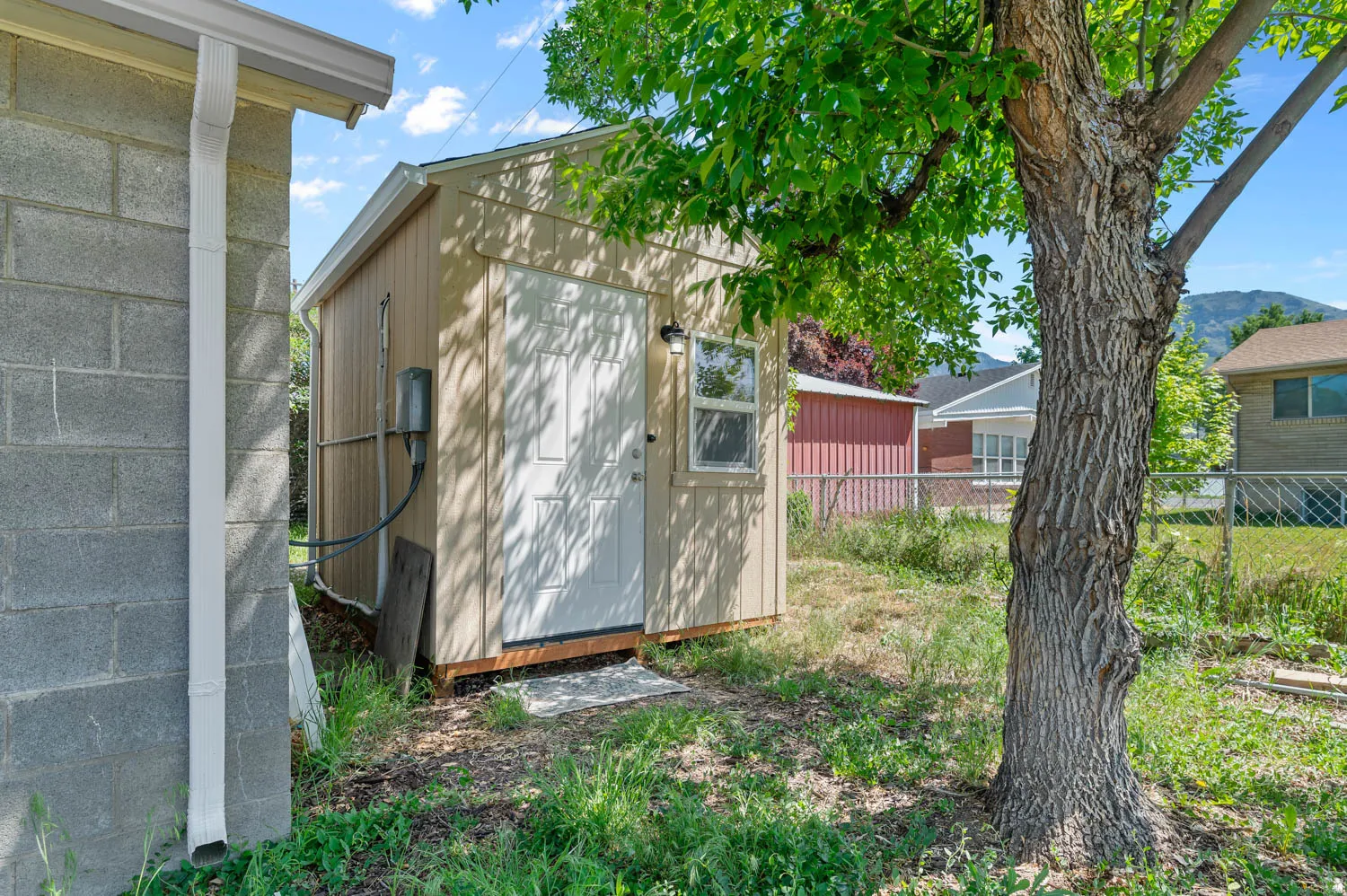 Utility shed featuring light-colored wood paneling, a white entry door, and a single window
